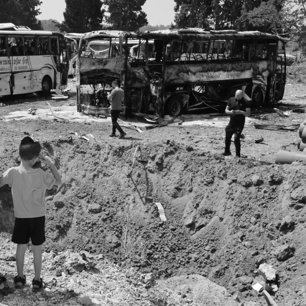 Onlookers stand in front of a crater at the impact site of an Iranian missile at a bus depot in Herzliya near Tel Aviv on 17 June 2025.