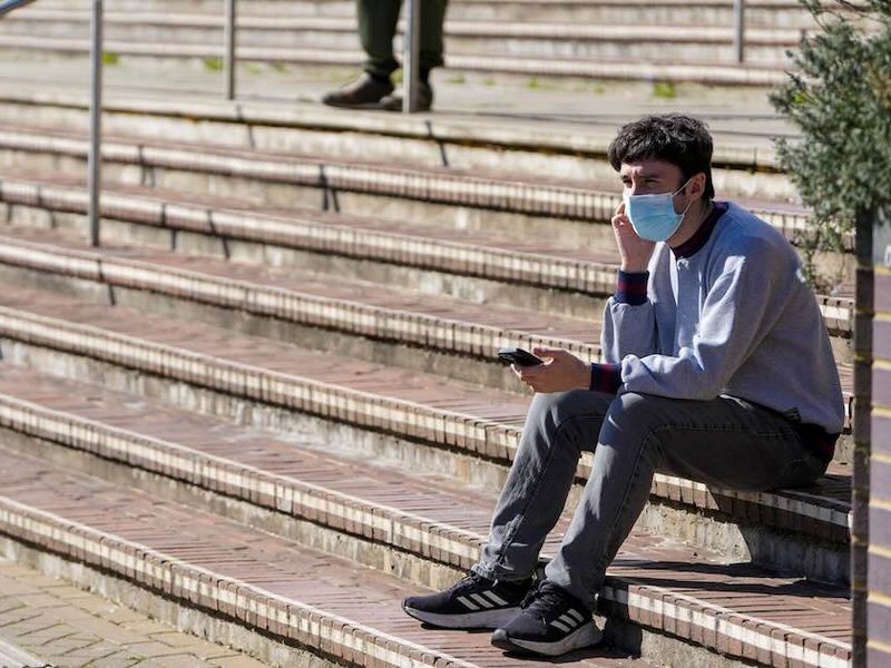 A man wearing a face mask sits on stairs at the University of Kent in Canterbury, following an outbreak of meningitis.