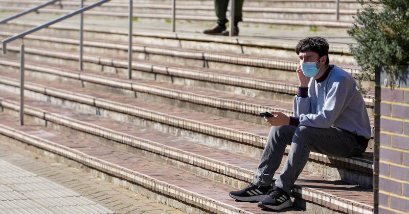 A man wearing a face mask sits on stairs at the University of Kent in Canterbury, following an outbreak of meningitis.