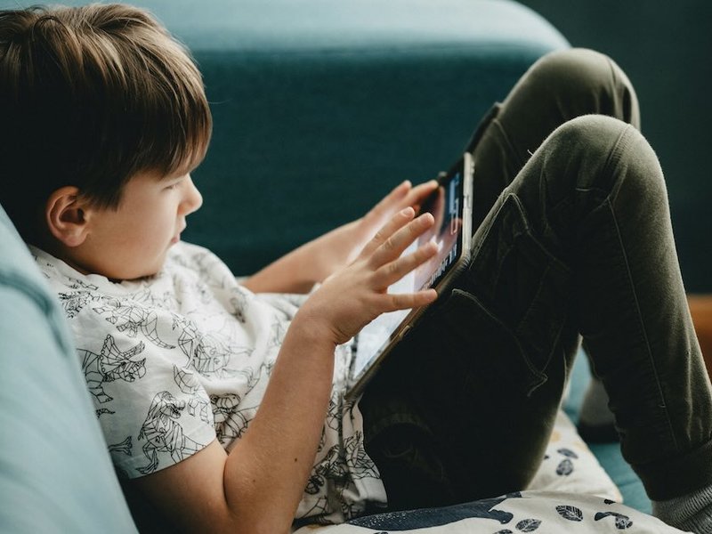 A young child using a tablet on a sofa