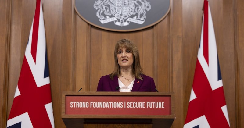 The chancellor Rachel Reeves standing at a podium between two Union Jacks. A sign on the podium reads “Strong foundations, secure future”.