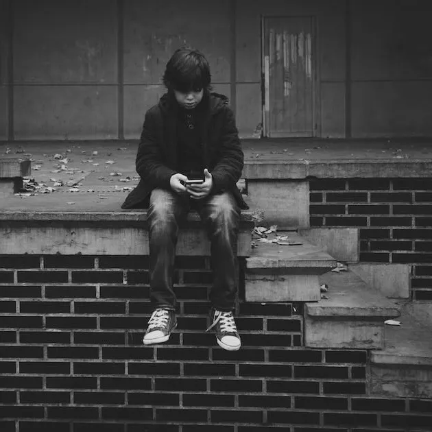 A boy sitting on steps looking at a phone