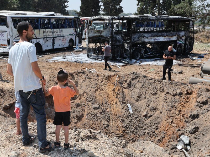 Onlookers stand in front of a crater at the impact site of an Iranian missile at a bus depot in Herzliya near Tel Aviv on 17 June 2025.