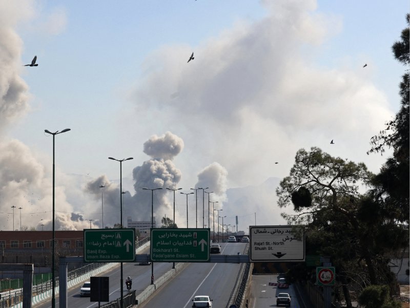 Vehicles drive along an expressway against the backdrop of smoke rising after a strike on the Iranian capital of Tehran on March 5, 2026.