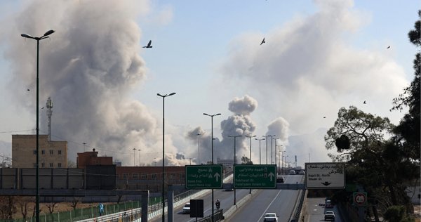 Vehicles drive along an expressway against the backdrop of smoke rising after a strike on the Iranian capital of Tehran on March 5, 2026.