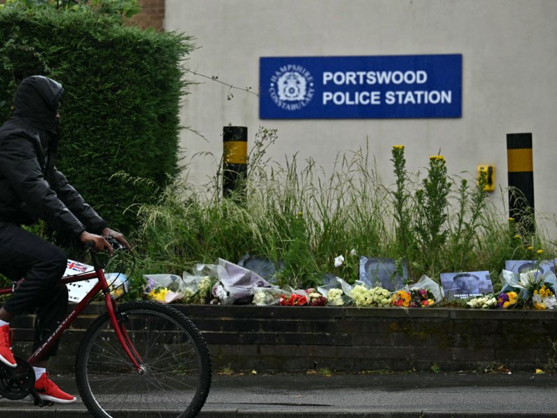 A picture of a person cycling past floral tributes for Henry Nowak outside of Portswood Police Station in Southampton.