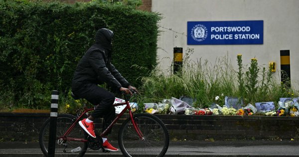 A picture of a person cycling past floral tributes for Henry Nowak outside of Portswood Police Station in Southampton.