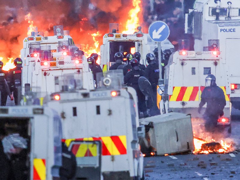 Fires burn around police vehicles as protesters (behind) stand off with police in Glengormley, north of Belfast, on 10 June.