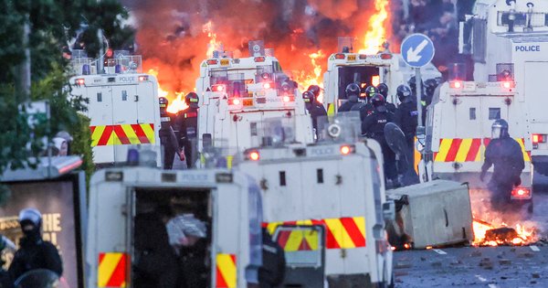 Fires burn around police vehicles as protesters (behind) stand off with police in Glengormley, north of Belfast, on 10 June.