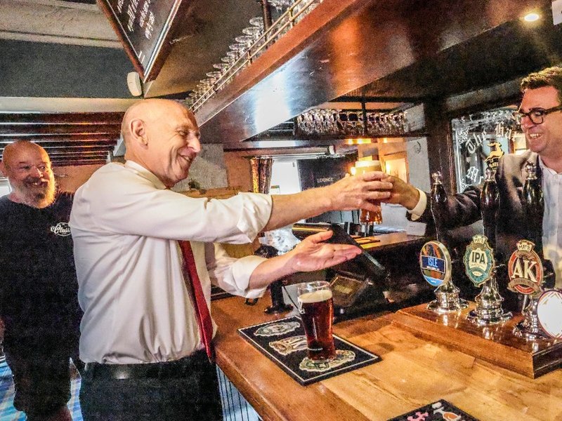 Prime Minister Andy Burnham handing Chancellor John Healey a pint during a visit to a pub.