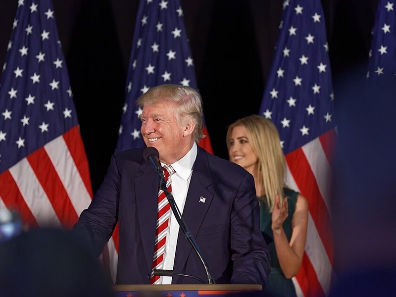 Donald Trump at a podium, his daughter Ivanka in the background