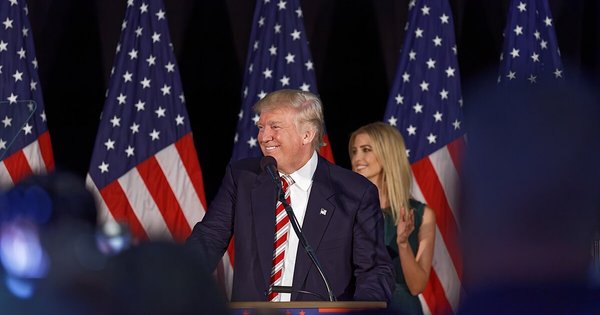 Donald Trump at a podium, his daughter Ivanka in the background