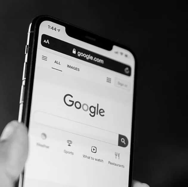 A person holding their phone showing the Google homepage, featuring the search bar.
