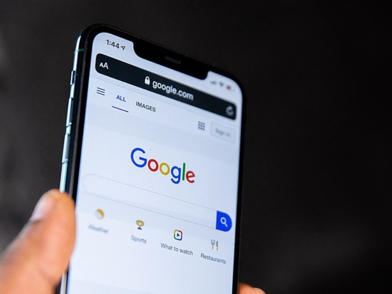 A person holding their phone showing the Google homepage, featuring the search bar.