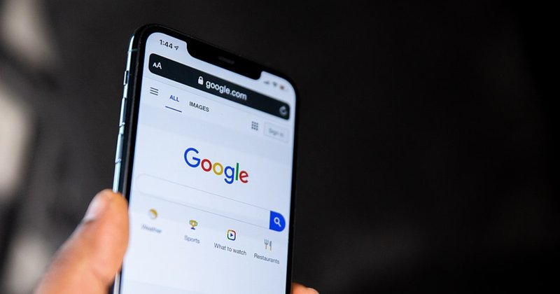 A person holding their phone showing the Google homepage, featuring the search bar.
