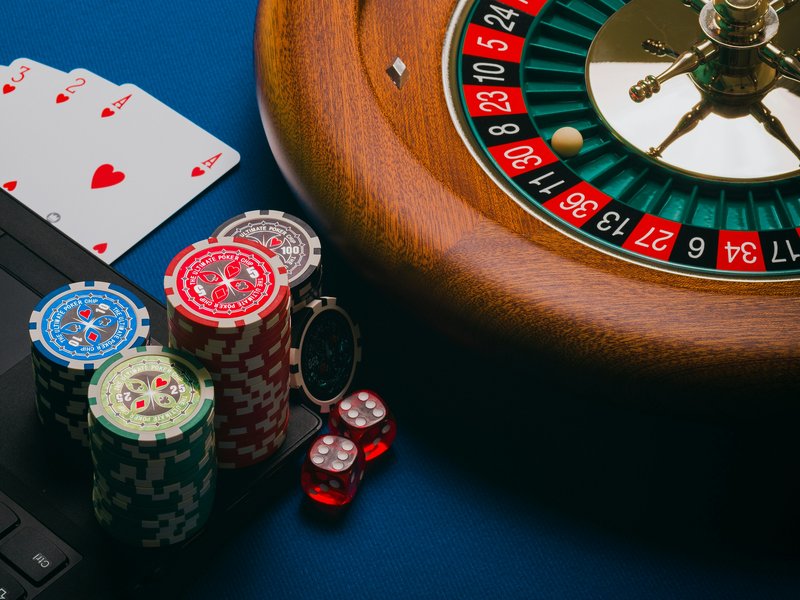 Image showing a laptop alongside cards, dice, roulette, poker chips.