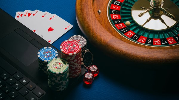 Image showing a laptop alongside cards, dice, roulette, poker chips.