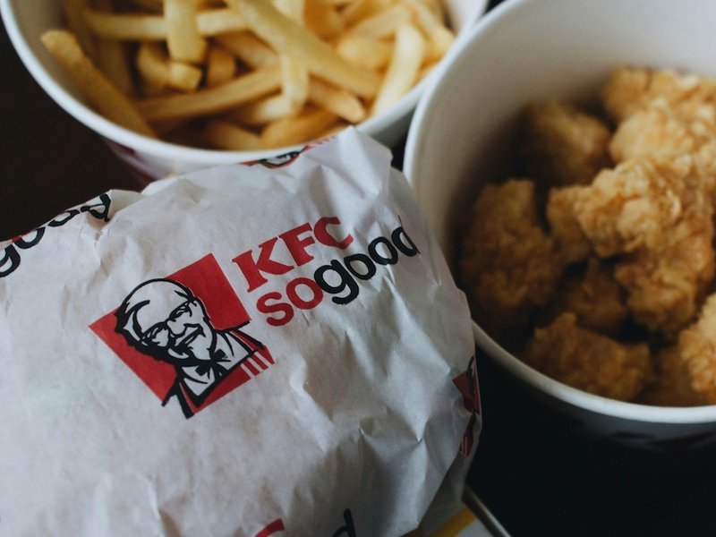 KFC branded wrapped sandwich beside chips and a small bucket of fried chicken