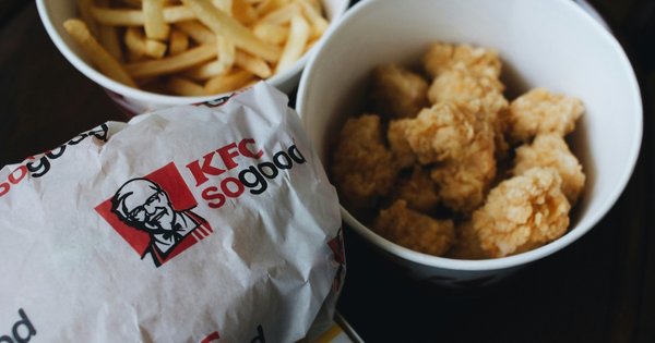 KFC branded wrapped sandwich beside chips and a small bucket of fried chicken
