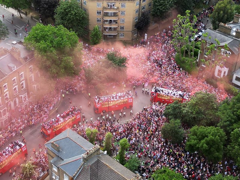 A bird’s eye view of four Arsenal open-top buses surrounded by fans and red smoke.