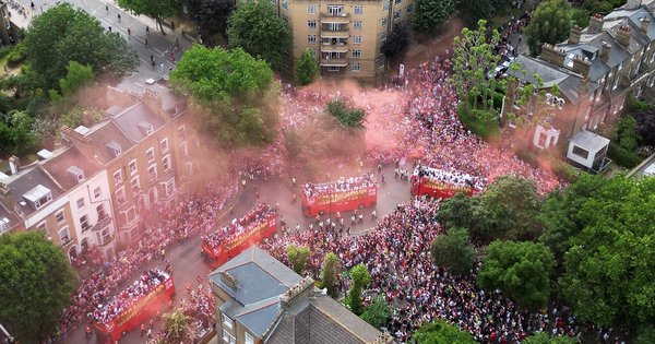 A bird’s eye view of four Arsenal open-top buses surrounded by fans and red smoke.