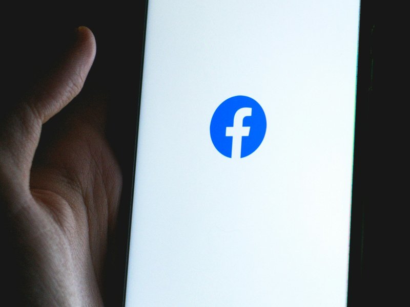 A hand holding a phone with the Facebook logo displayed on the screen
