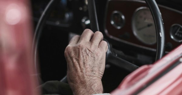 An older man’s hand on the steering wheel of a car.