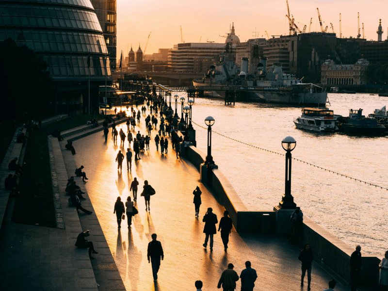 A photo taken at sunset of people walking by the Thames in London