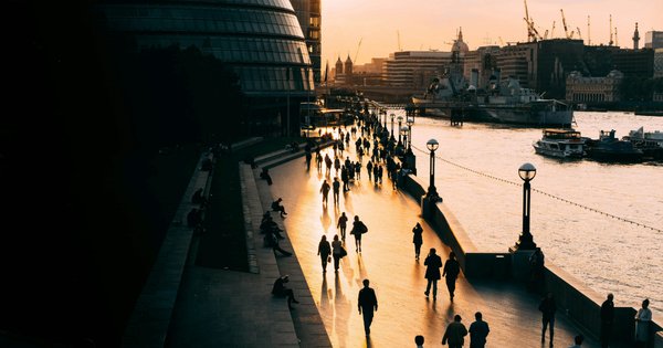 A photo taken at sunset of people walking by the Thames in London