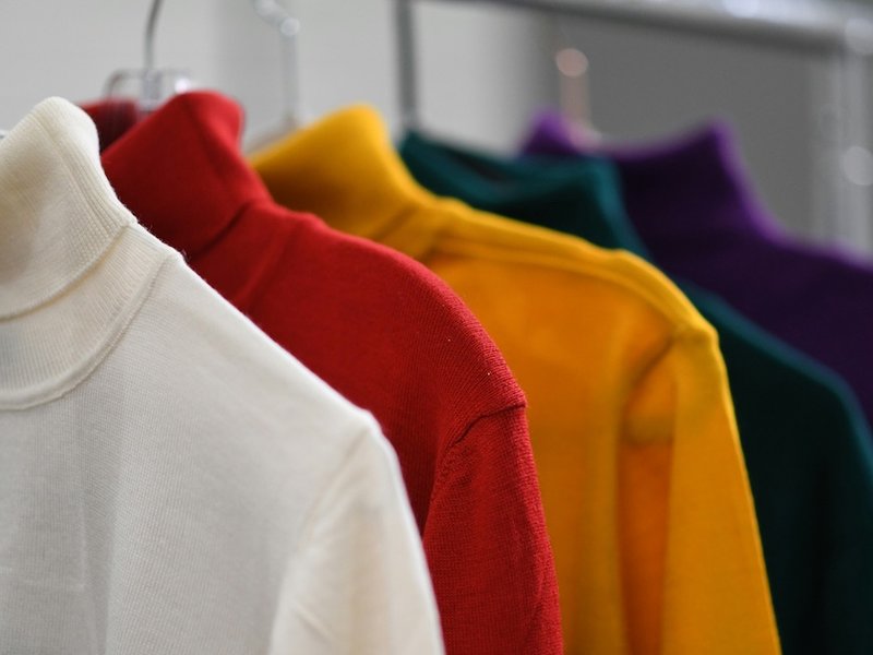 White, red, yellow, green and purple polo neck jumpers hanging in a row.