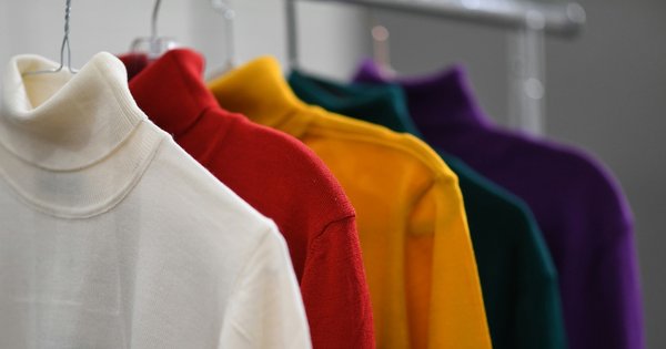 White, red, yellow, green and purple polo neck jumpers hanging in a row.