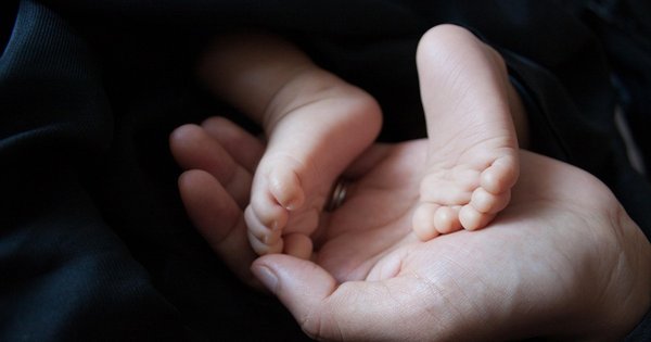 A hand holding a newborn baby's feet