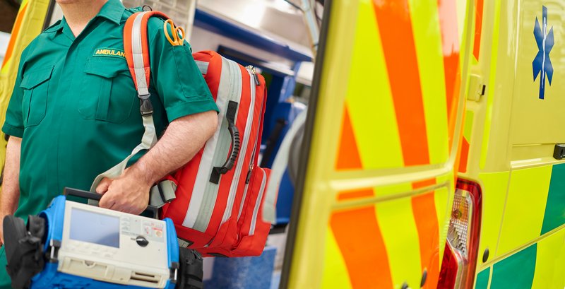 A paramedic holding medical equipment stood behind the rear doors of an ambulance.