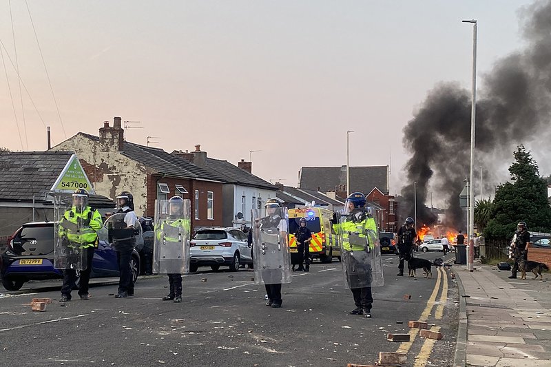 Smoke billows from a fire started by protesters as riot police stand guard after disturbances near the Southport Islamic Society Mosque in Southport, northwest England, on July 30, 2024, a day after a deadly child knife attack