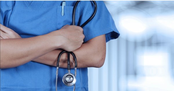 A person wearing blue medical scrubs with their arms folded and holding a stethoscope.